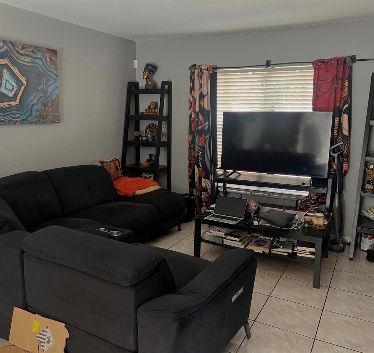 A living room with a black sectional sofa, a television on a stand, and shelving units — MIAMI GARDENS, FL