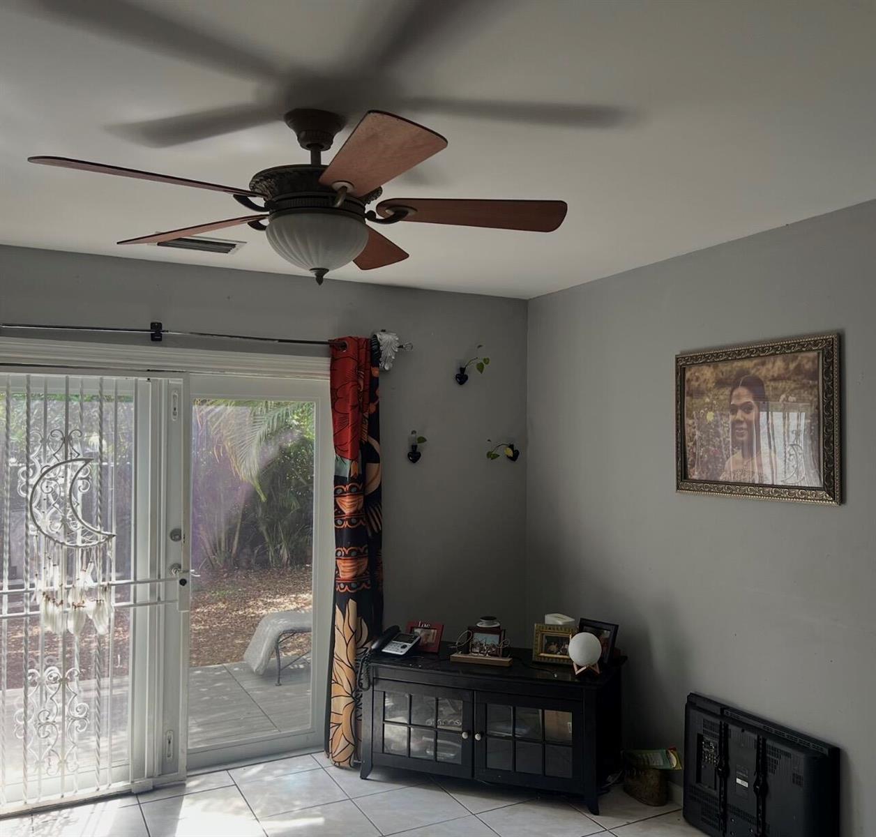 A room with a ceiling fan, sliding glass doors, a black cabinet, and wall art — MIAMI GARDENS, FL