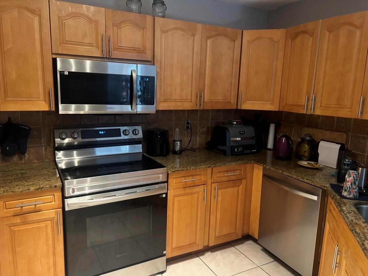 A kitchen features light wood cabinets, granite countertops, and stainless steel appliances — MIAMI GARDENS, FL