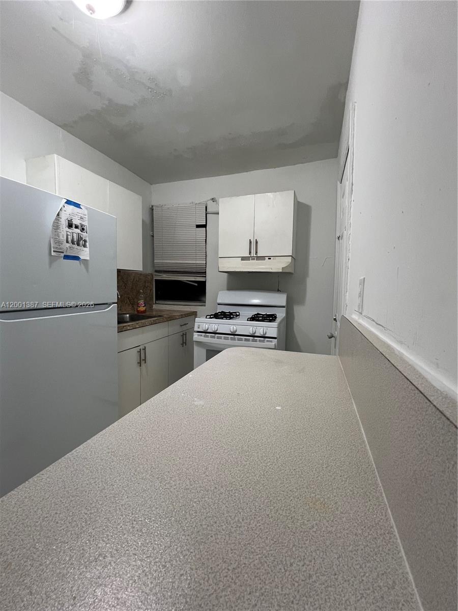 A small kitchen features white cabinets, a white refrigerator, a gas stove, and laminate countertops — 413 NW 33rd St # A, Miami FL 33127, MIAMI, FL