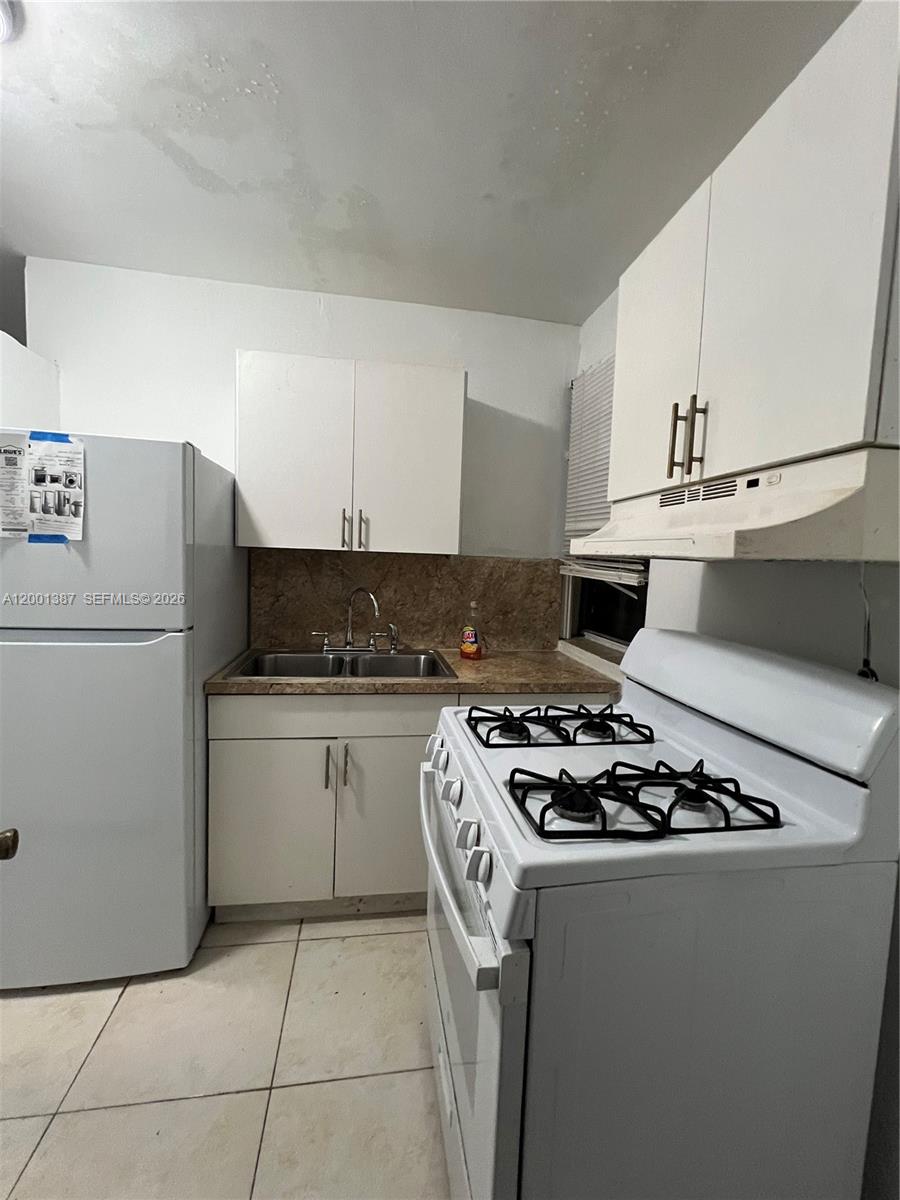 A small kitchen features white cabinets, a white stove, a refrigerator, and a double sink — 413 NW 33rd St # A, Miami FL 33127, MIAMI, FL