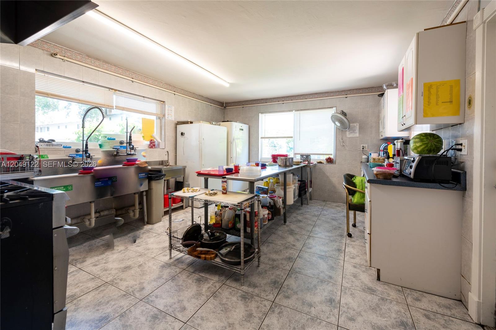 A commercial kitchen features stainless steel prep tables, a multi-basin sink, and tiled flooring — 1930 Lincoln St, Hollywood FL 33020, HOLLYWOOD, FL