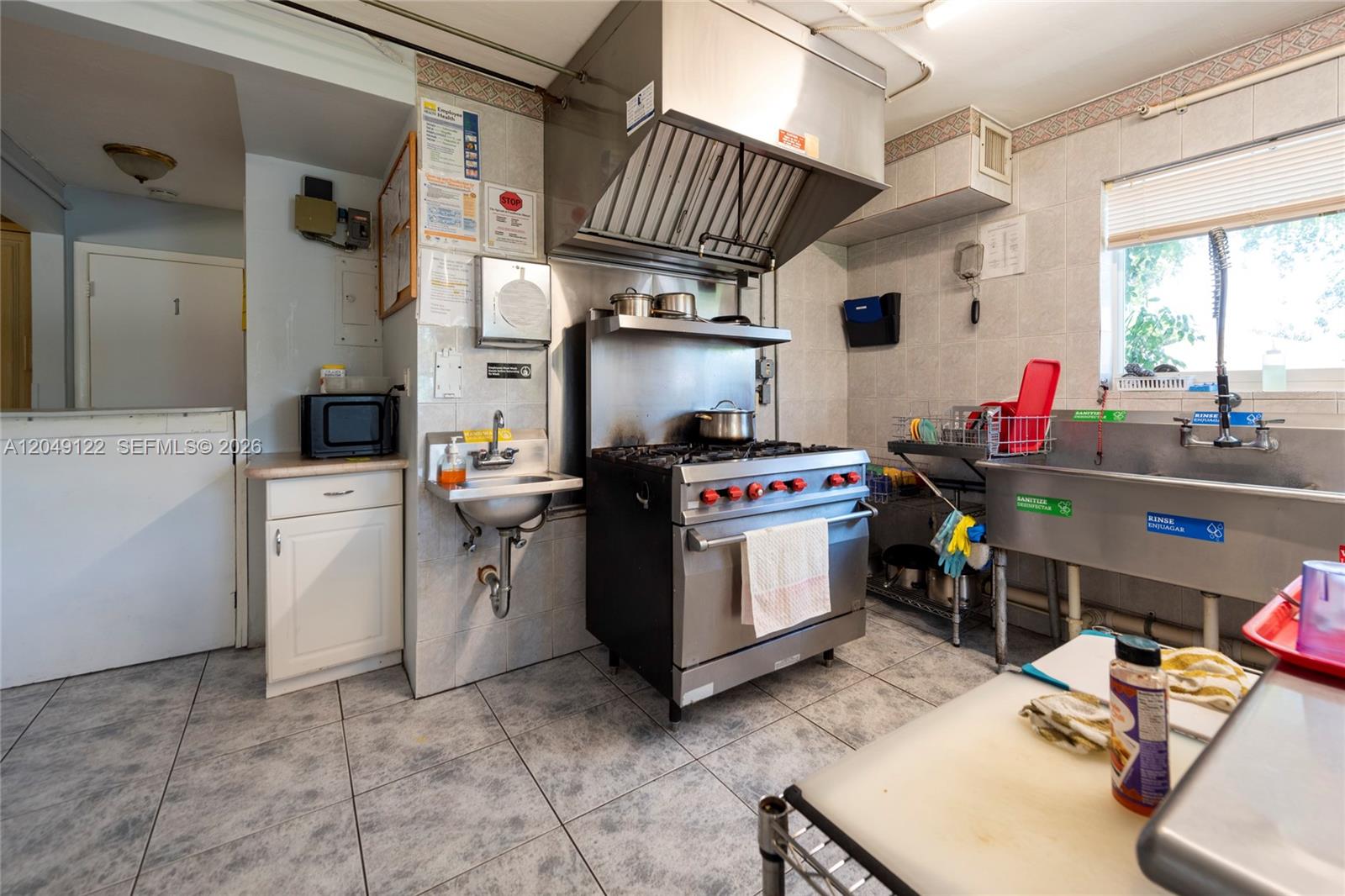 A commercial kitchen features a stainless steel stove, a vent hood, and a utility sink — 1930 Lincoln St, Hollywood FL 33020, HOLLYWOOD, FL