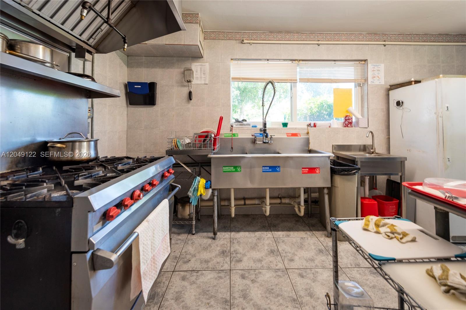 A commercial kitchen features a large stainless steel stove, a three-compartment sink, and tile flooring — 1930 Lincoln St, Hollywood FL 33020, HOLLYWOOD, FL