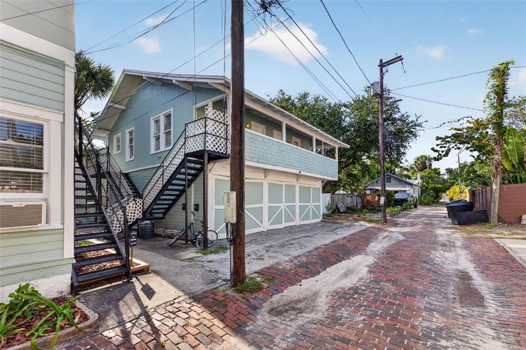 A two-story light blue house with an external staircase sits beside a brick alleyway — 633 7TH AVENUE N, ST PETERSBURG, FL