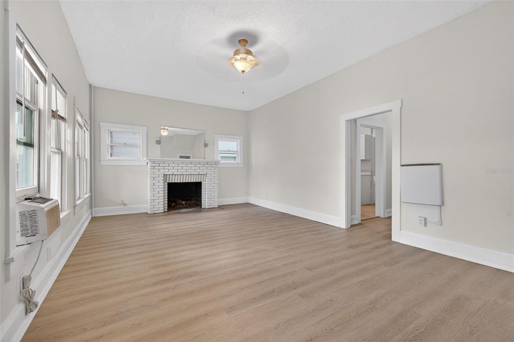 A living room features light wood-look flooring, a white brick fireplace, and a ceiling fan — 633 7TH AVENUE N, ST PETERSBURG, FL