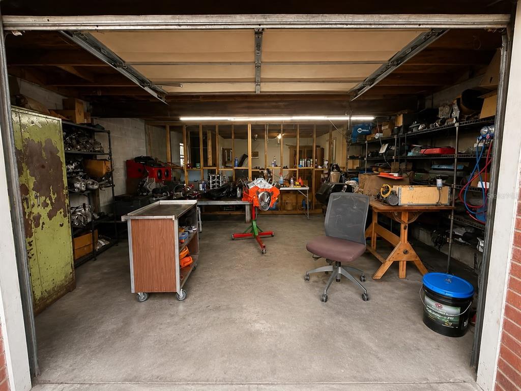 A cluttered garage workspace features an engine on a stand, metal shelving, and concrete floors — 2504 S 54TH STREET, TAMPA, FL