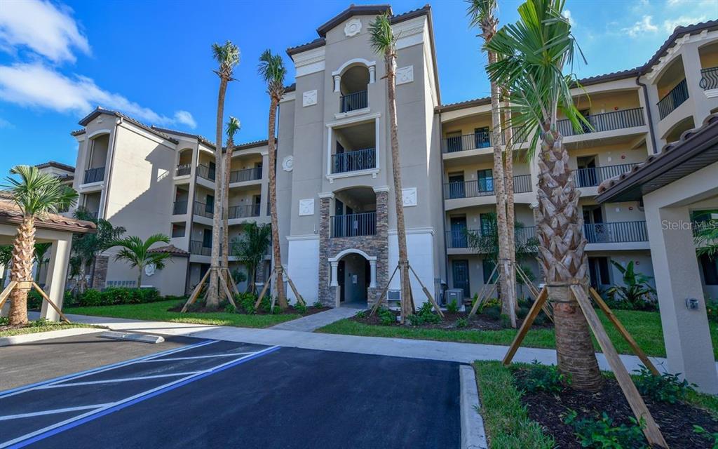A multi-story apartment building exterior with palm trees and a paved parking area in front — 17006 VARDON TERRACE UNIT 208, BRADENTON, FL
