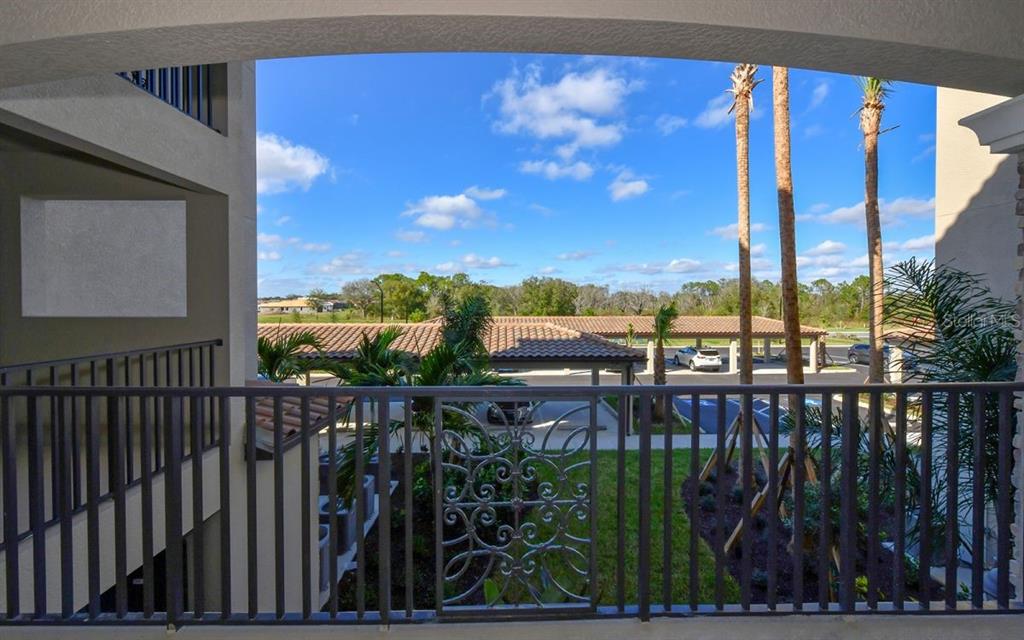 A view from a balcony overlooking a parking area with palm trees and a blue sky — 17006 VARDON TERRACE UNIT 208, BRADENTON, FL