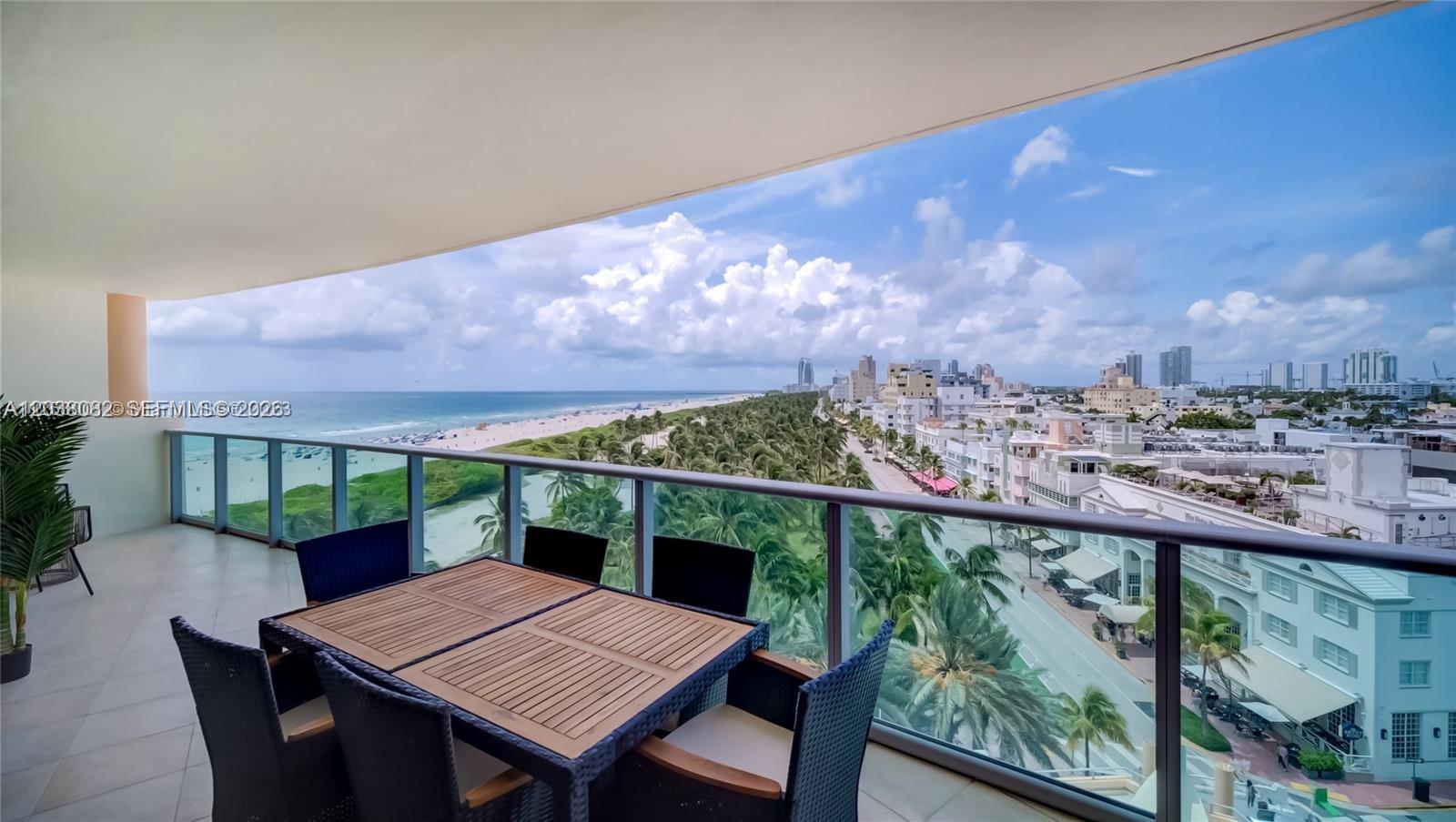 A balcony with outdoor dining furniture overlooks a beach, palm trees, and a city skyline — 1455 Ocean Dr # 902, Miami Beach FL 33139, MIAMI BEACH, FL