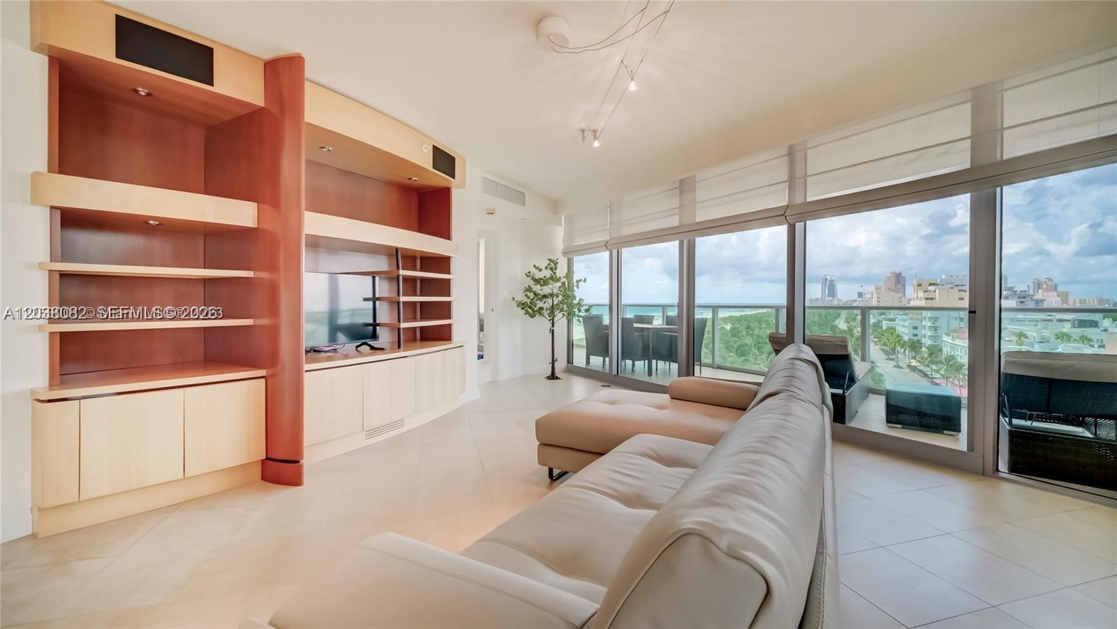 A living room features a large built-in entertainment unit, a sectional sofa, and floor-to-ceiling windows — 1455 Ocean Dr # 902, Miami Beach FL 33139, MIAMI BEACH, FL