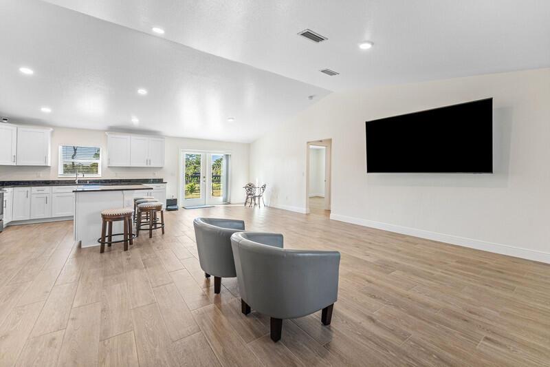 An open-concept living area features a kitchen with white cabinets and a wall-mounted television — 18476 40th Run N, Loxahatchee FL 33470, LOXAHATCHEE, FL