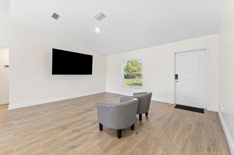 A living room features light wood-look flooring, white walls, a mounted television, and two chairs — 18476 40th Run N, Loxahatchee FL 33470, LOXAHATCHEE, FL