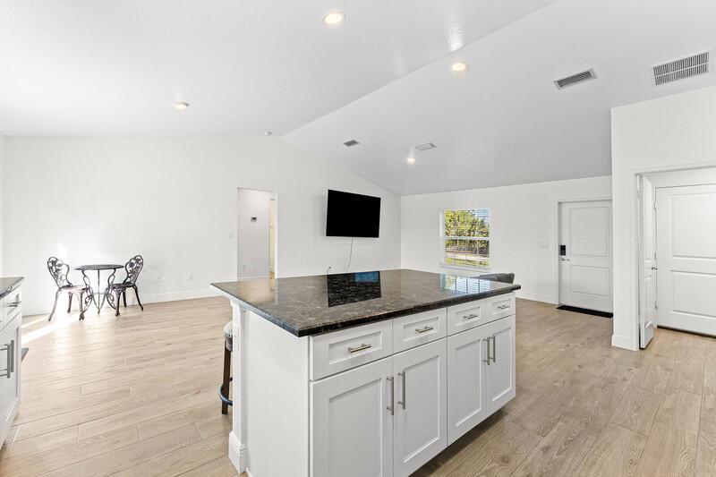A kitchen island with a dark granite countertop sits in a bright, open-concept living space — 18476 40th Run N, Loxahatchee FL 33470, LOXAHATCHEE, FL