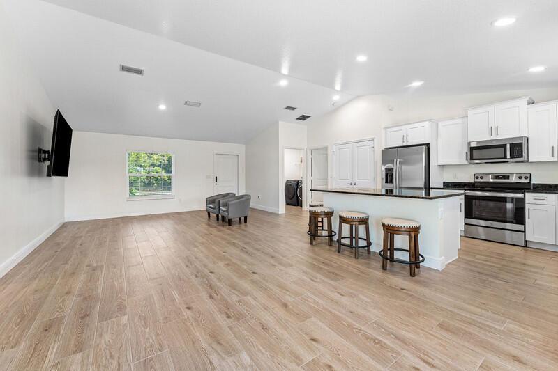 An open-concept kitchen and living area features light wood-look tile flooring and white cabinetry — 18476 40th Run N, Loxahatchee FL 33470, LOXAHATCHEE, FL