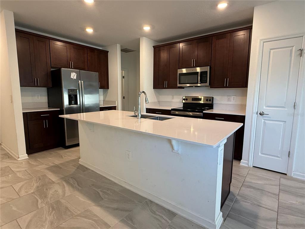 A kitchen features dark wood cabinets, stainless steel appliances, a white island, and tiled flooring — 558 JETT LANE, DAVENPORT, FL
