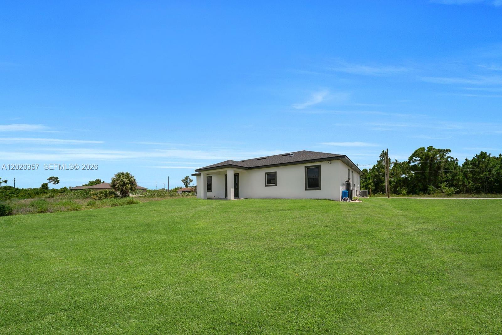 A single-story house with a white exterior sits on a large, grassy lot — 3114 39TH ST SW, Lehigh Acres FL 33976, LEHIGH ACRES, FL
