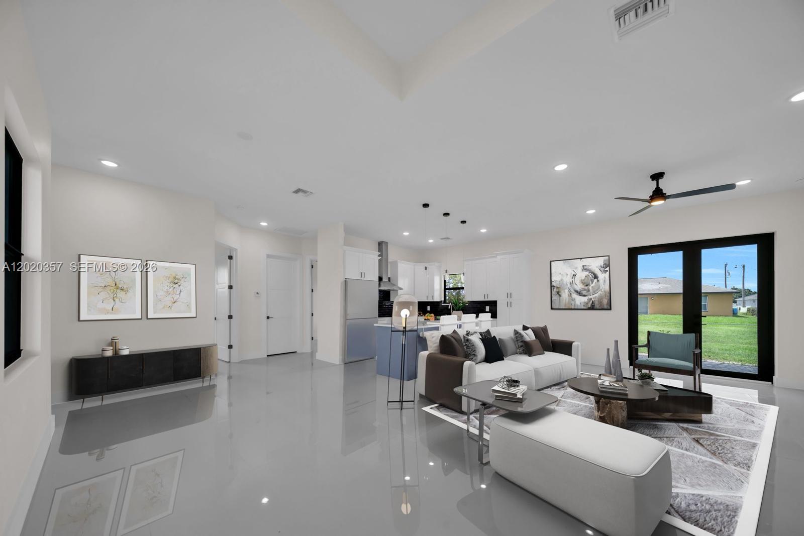A modern open-concept living room and kitchen featuring white cabinetry, gray tile flooring, and furniture — 3114 39TH ST SW, Lehigh Acres FL 33976, LEHIGH ACRES, FL