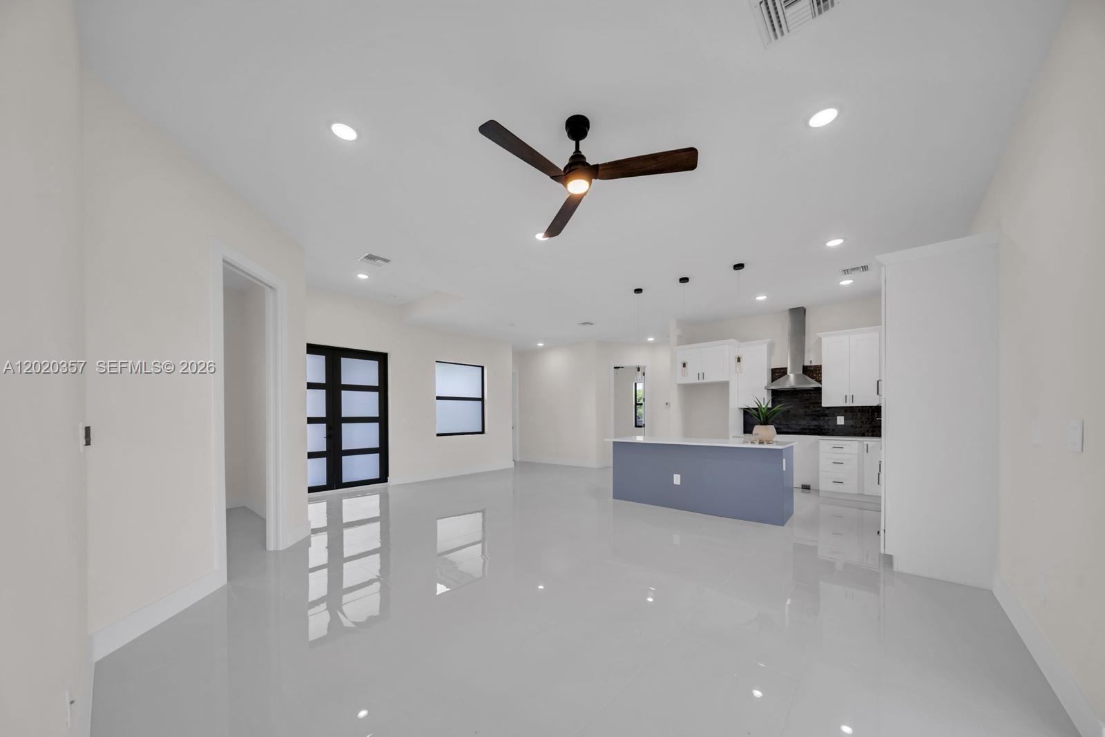 An open-concept kitchen and living area features white walls, glossy tile floors, and a blue island — 3114 39TH ST SW, Lehigh Acres FL 33976, LEHIGH ACRES, FL
