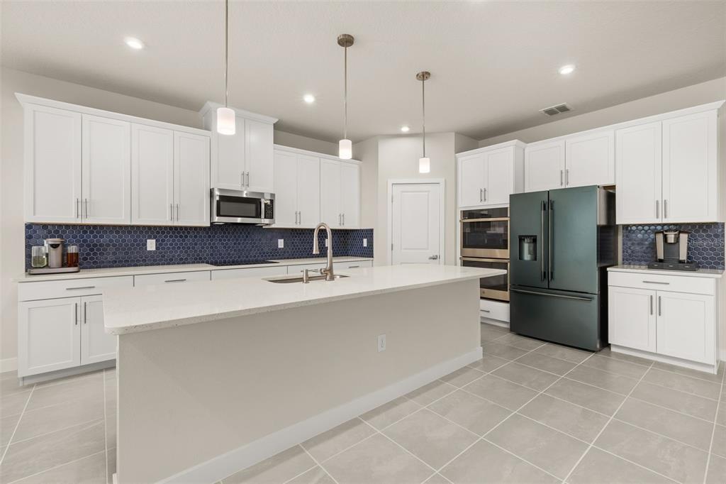 A modern kitchen features white cabinets, a large island, stainless appliances, and a blue backsplash — 11182 NELLIE CROSSING CIRCLE, CLERMONT, FL