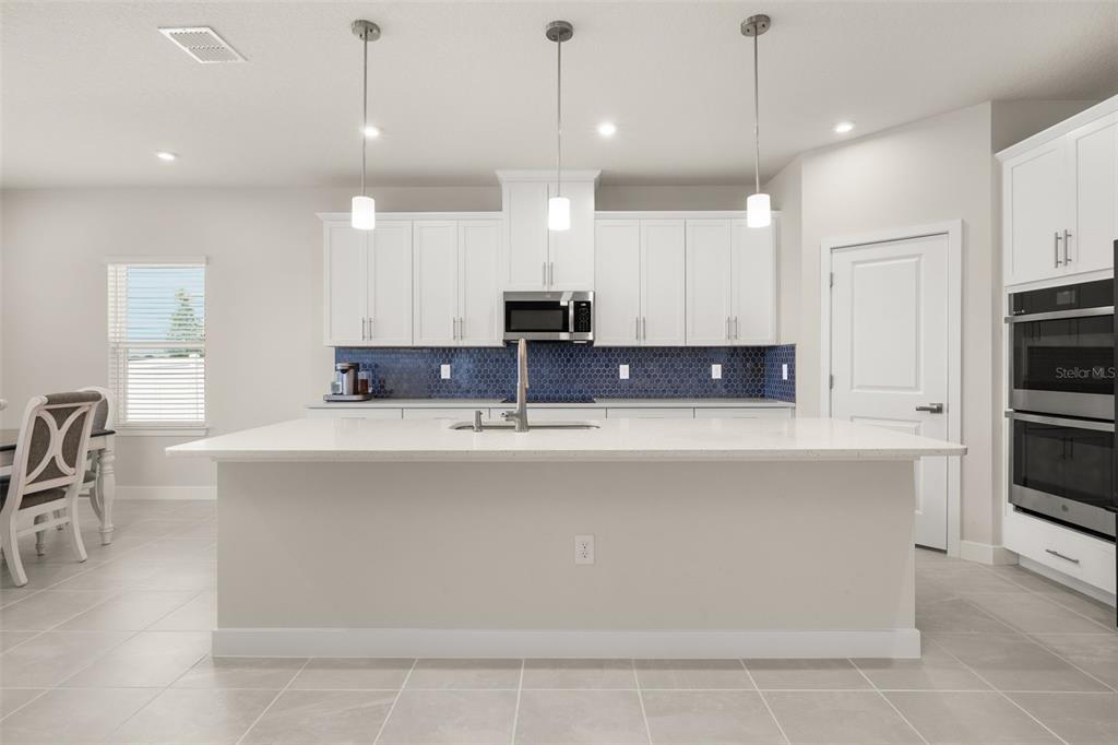 A modern kitchen features white cabinetry, a large central island, and a blue tiled backsplash — 11182 NELLIE CROSSING CIRCLE, CLERMONT, FL