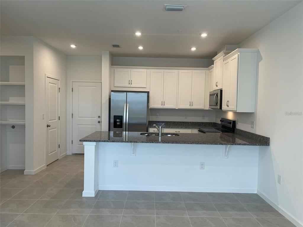 A kitchen features white cabinets, granite countertops, a stainless steel refrigerator, and tile flooring — 3107 GARDENIA RESERVE STREET, APOPKA, FL