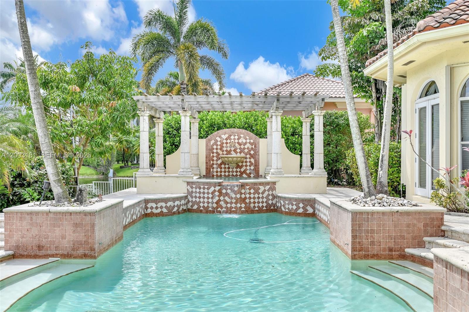 A swimming pool features a decorative tiled fountain wall and a wooden pergola — 10430 Kestrel St, Plantation FL 33324, PLANTATION, FL
