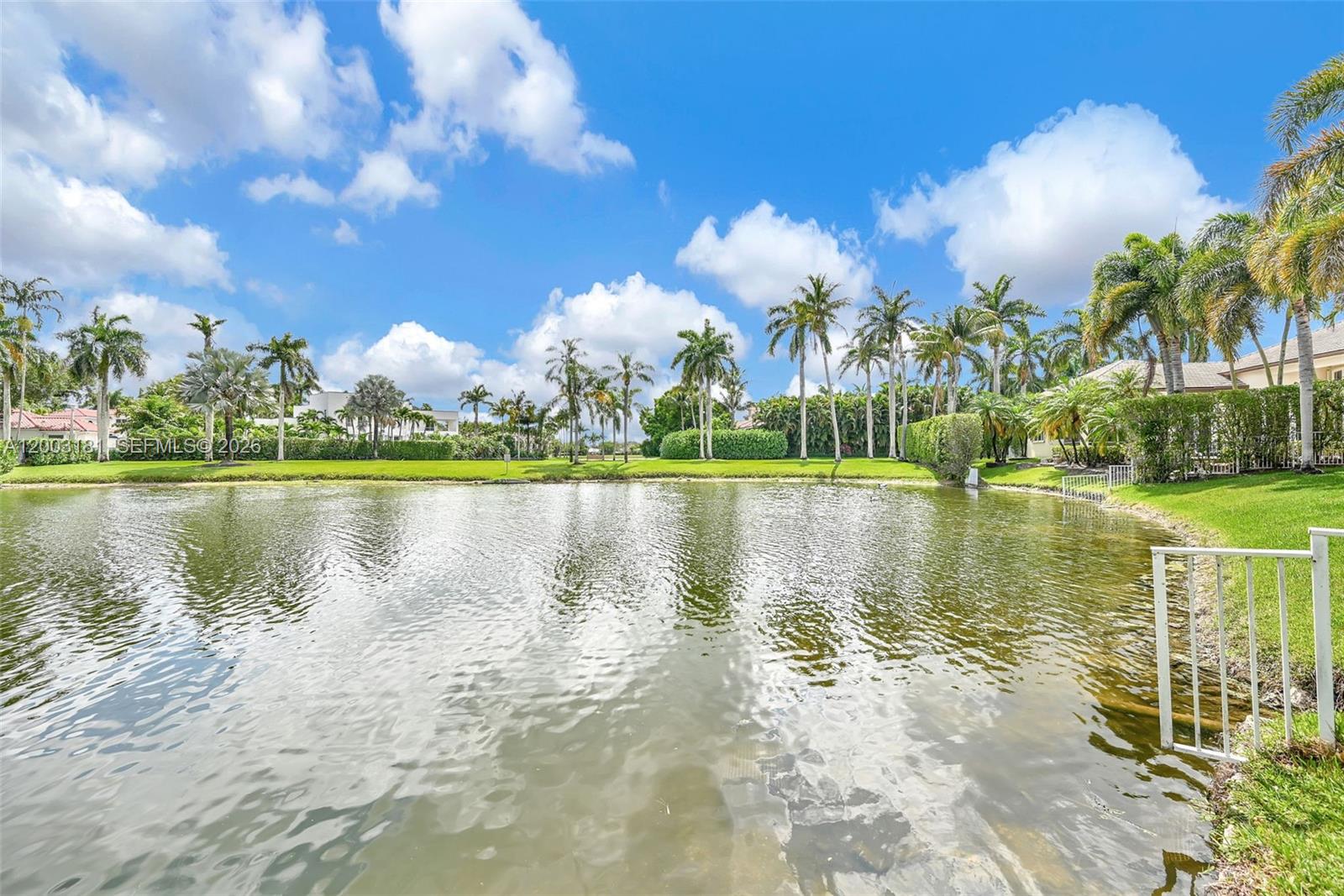 A pond sits in front of a grassy lawn lined with palm trees and houses — 10430 Kestrel St, Plantation FL 33324, PLANTATION, FL