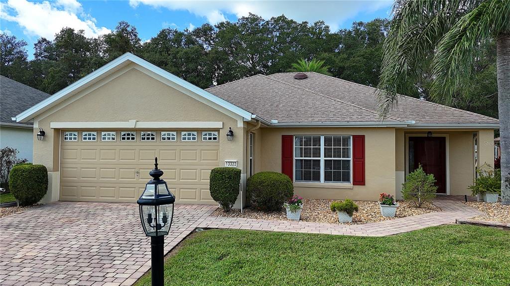 A single-story tan house with a two-car garage, red shutters, and a paved driveway — 13322 SE 86TH CIRCLE, SUMMERFIELD, FL