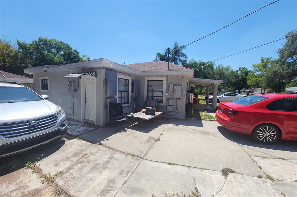 A gray house exterior features a concrete driveway, two parked cars, and several electrical boxes — 6809 N GUNLOCK AVENUE, TAMPA, FL