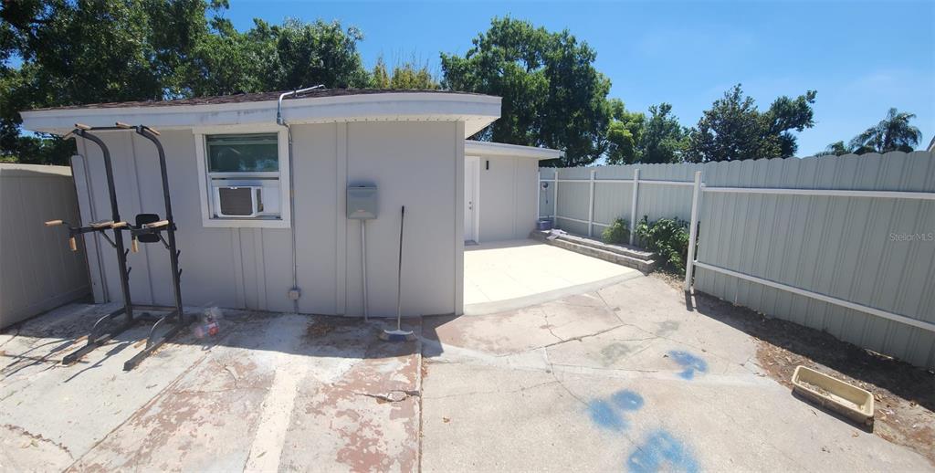 A concrete patio area sits beside a small, light-colored building with a window air conditioner — 6809 N GUNLOCK AVENUE, TAMPA, FL