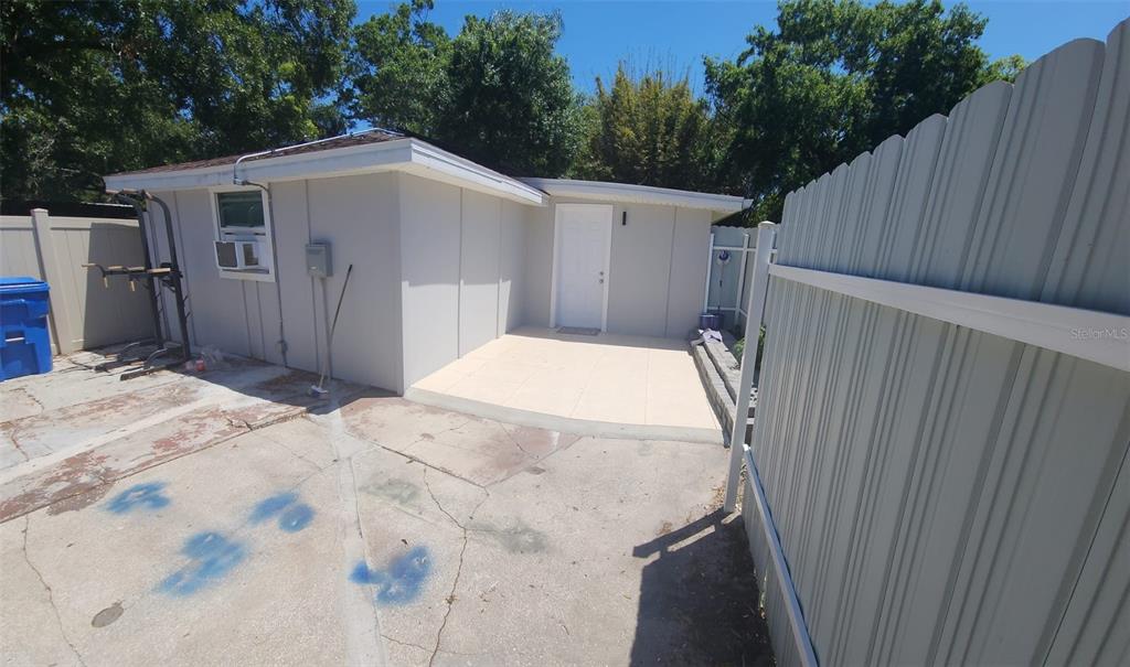 A small, light-colored detached building with a white door and a concrete patio area — 6809 N GUNLOCK AVENUE, TAMPA, FL