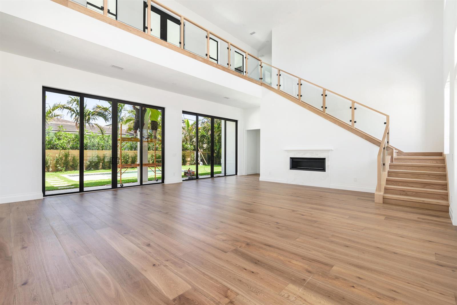 A spacious living room features light wood floors, a glass-railed staircase, and large sliding doors — 261 Rutland Boulevard, West Palm Beach FL 33405, WEST PALM BEACH, FL