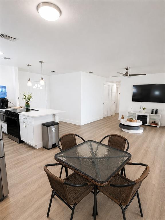 An open-concept kitchen and living area features light wood flooring, white cabinetry, and a dining set — 11105 N 22ND STREET, TAMPA, FL