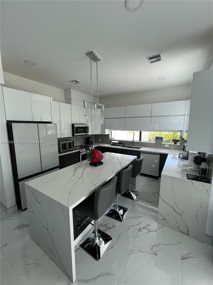 A modern kitchen features white high-gloss cabinets, a marble-patterned island, and gray bar stools — 2342 Mckinley St # 3, Hollywood FL 33020, HOLLYWOOD, FL