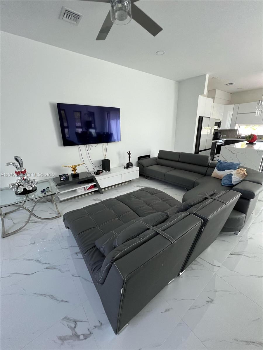 A modern living room features a grey sectional sofa, white tile floors, and a wall-mounted television — 2342 Mckinley St # 3, Hollywood FL 33020, HOLLYWOOD, FL