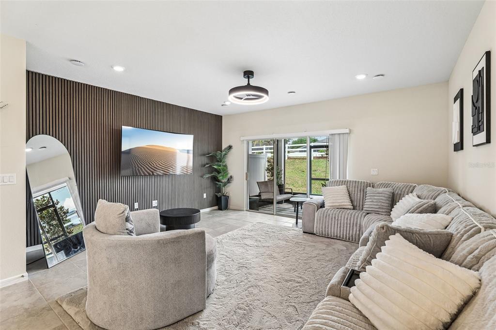 A living room features a dark wood-slat accent wall, a large sectional, and sliding doors — 2570 WINSOME WAY, DAVENPORT, FL