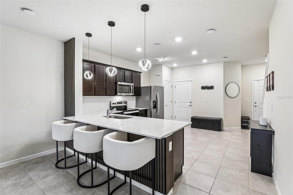 A modern kitchen features dark wood cabinets, a white quartz island, and three bar stools — 2570 WINSOME WAY, DAVENPORT, FL