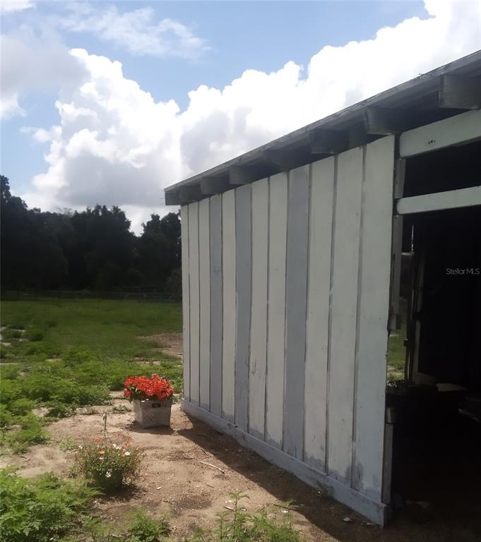 A side view of a wooden shed with vertical siding and a partial open entrance — 17936 SE 95TH STREET ROAD, OCKLAWAHA, FL