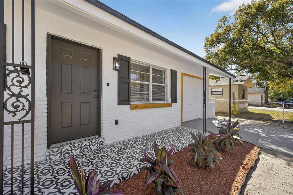 A white brick house exterior features a patterned tile porch, dark shutters, and a front door — 8309 TUPELO DRIVE, TAMPA, FL