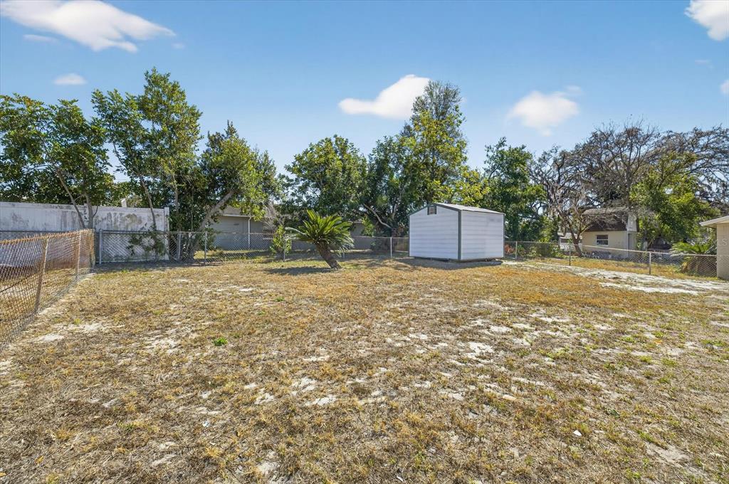 A fenced backyard features sparse grass, a small shed, and several mature trees — 8309 TUPELO DRIVE, TAMPA, FL
