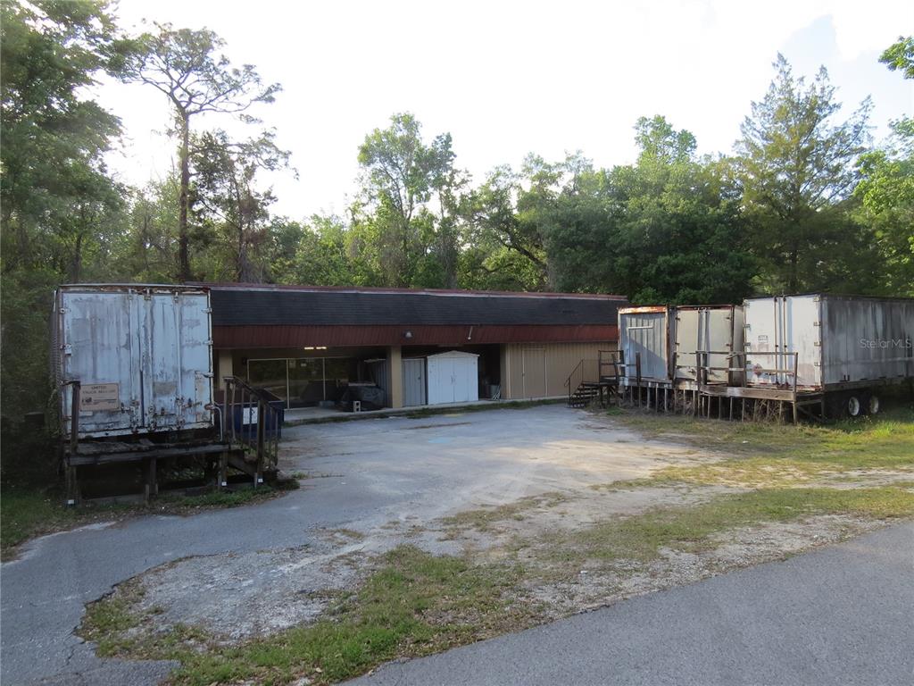 A single-story commercial building features a paved lot with three detached shipping containers on platforms — 28380 FORBES STREET, NOBLETON, FL