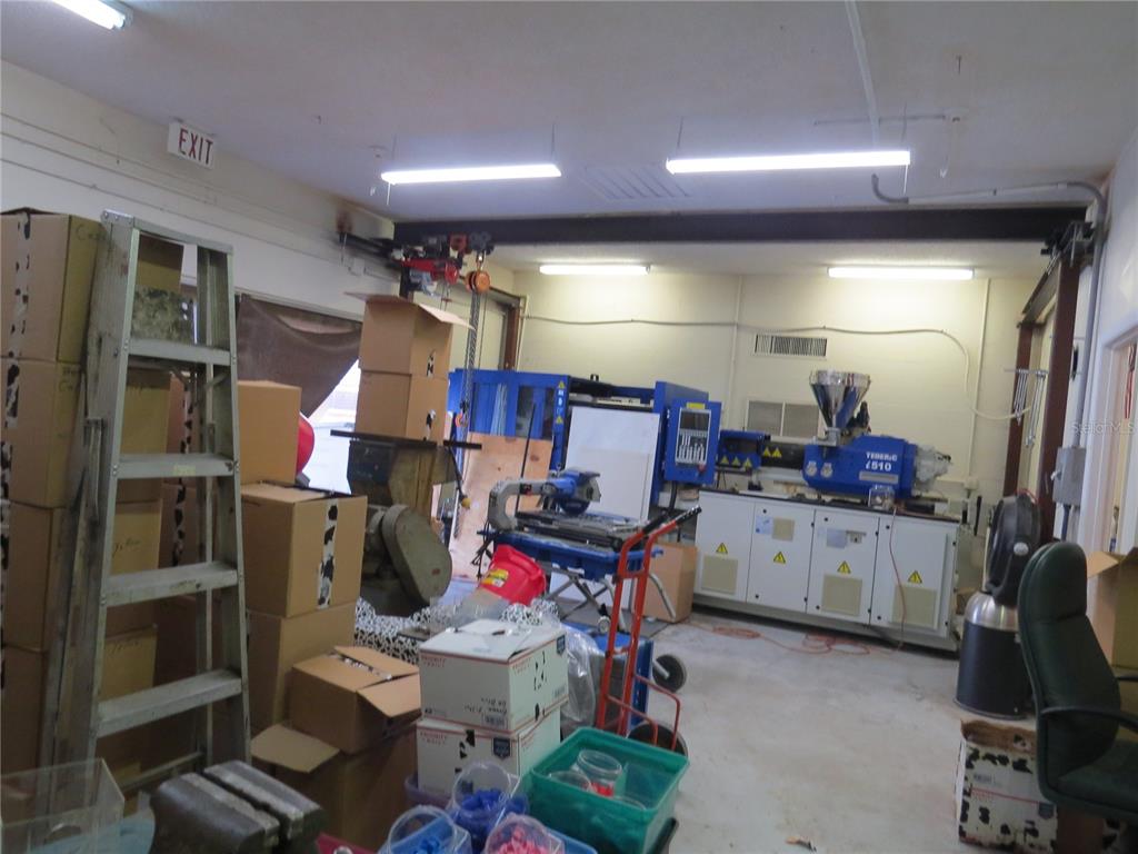 A cluttered industrial workshop features a large blue injection molding machine and stacks of boxes — 28380 FORBES STREET, NOBLETON, FL