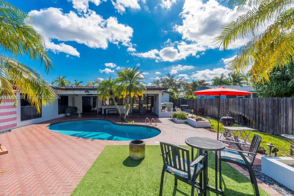 A backyard features a swimming pool, brick patio, artificial turf, and a red patio umbrella — 5201 Jefferson St, Hollywood FL 33021, HOLLYWOOD, FL