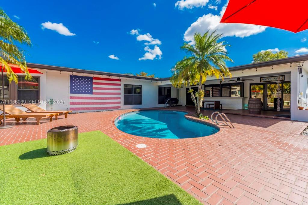 A backyard patio features a swimming pool, brick pavers, a fire pit, and an American flag — 5201 Jefferson St, Hollywood FL 33021, HOLLYWOOD, FL