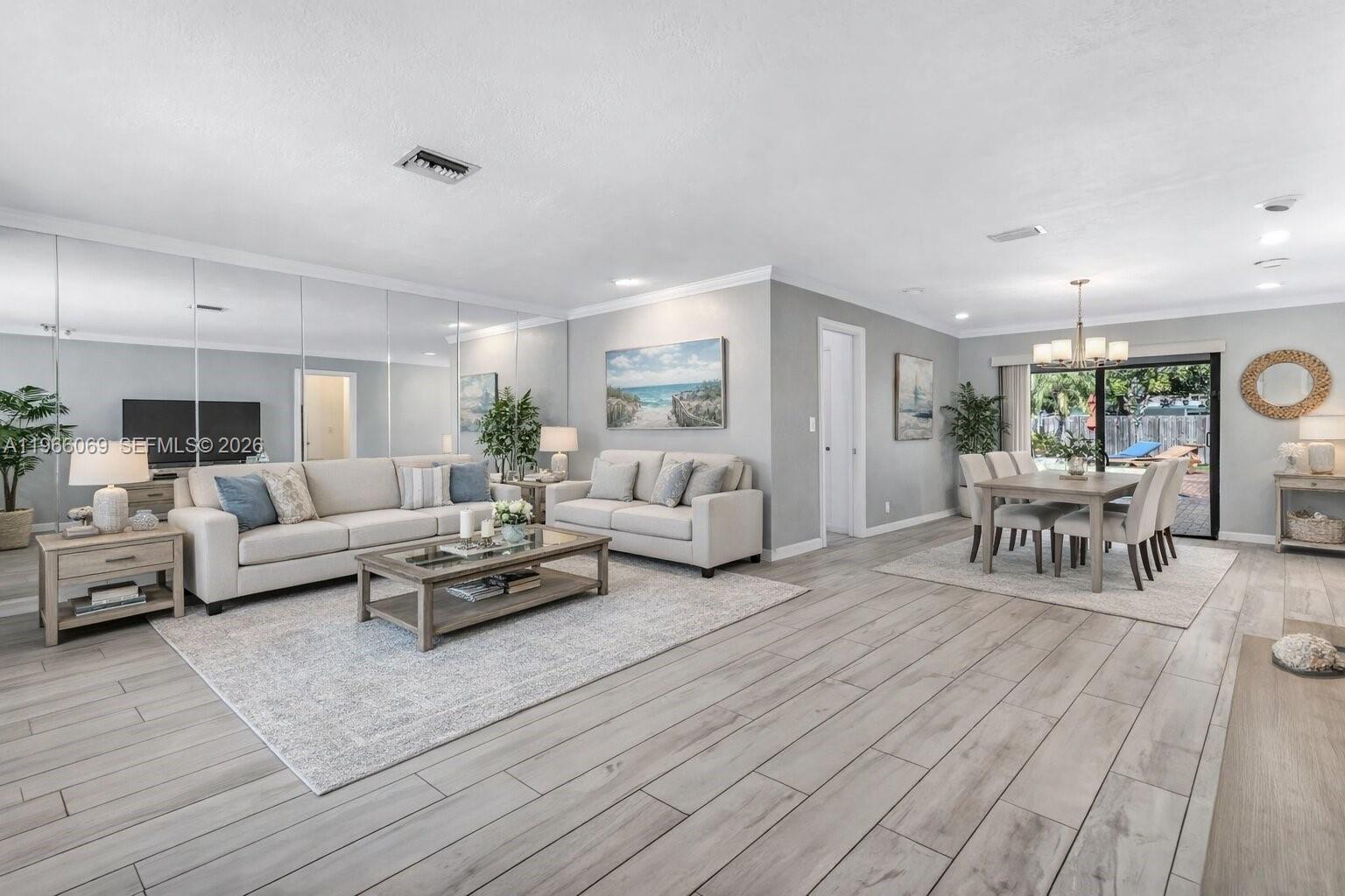 A living and dining room with light wood-look flooring, mirrored walls, and neutral furniture — 5201 Jefferson St, Hollywood FL 33021, HOLLYWOOD, FL