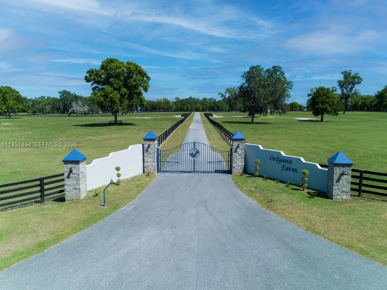 An aerial view shows a paved driveway leading to a gated entrance at Orlyana Farm — 7787 NW 150TH AVE, Ocala FL 32668, OCALA, FL