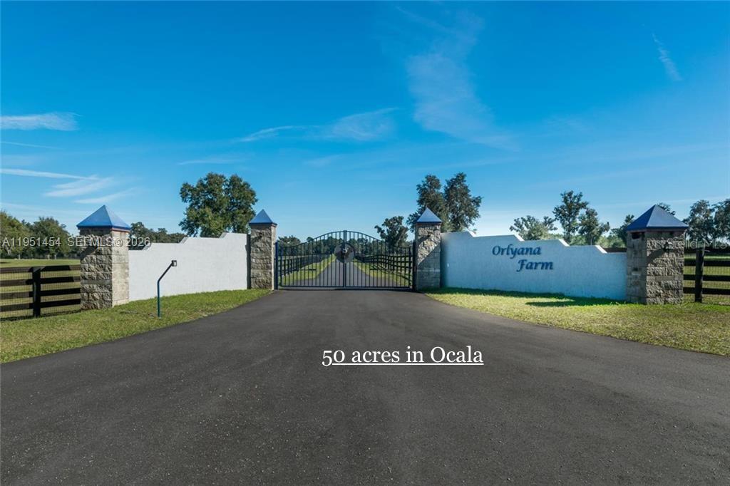 A paved driveway leads to a gated entrance with stone pillars and white walls — 7787 NW 150TH AVE, Ocala FL 32668, OCALA, FL