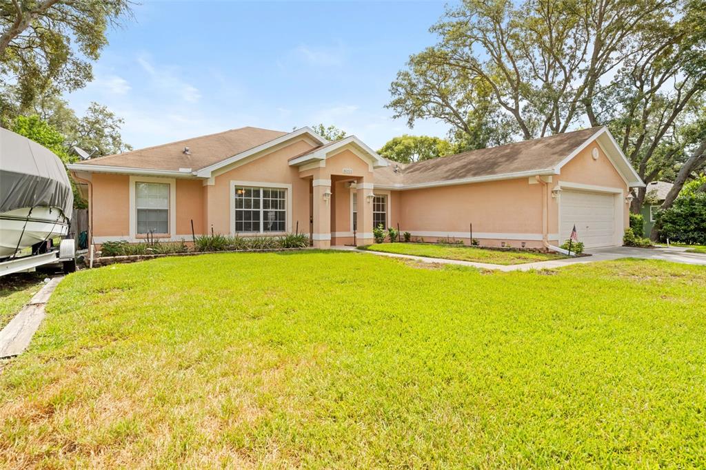 A single-story peach-colored house with a front lawn, a two-car garage, and a boat parked — 8053 TIMBERLAKE AVENUE, SPRING HILL, FL