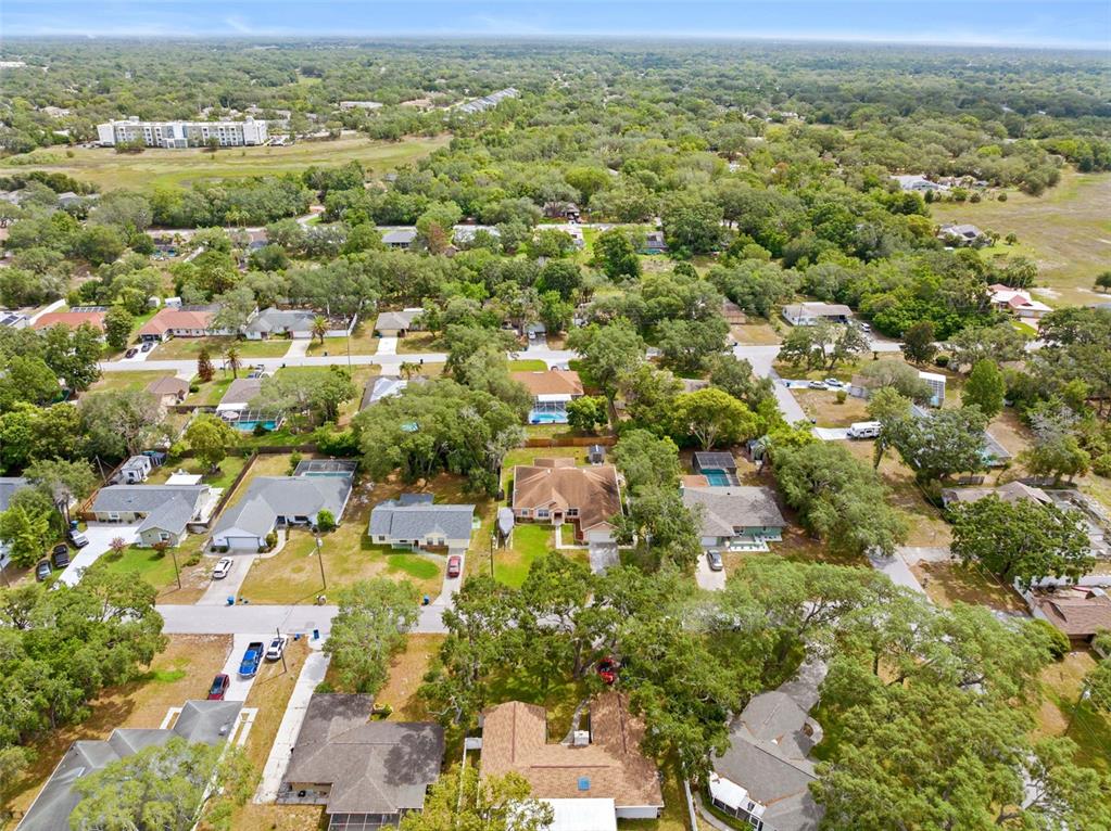 An aerial view shows a suburban neighborhood with single-family homes, mature trees, and streets — 8053 TIMBERLAKE AVENUE, SPRING HILL, FL